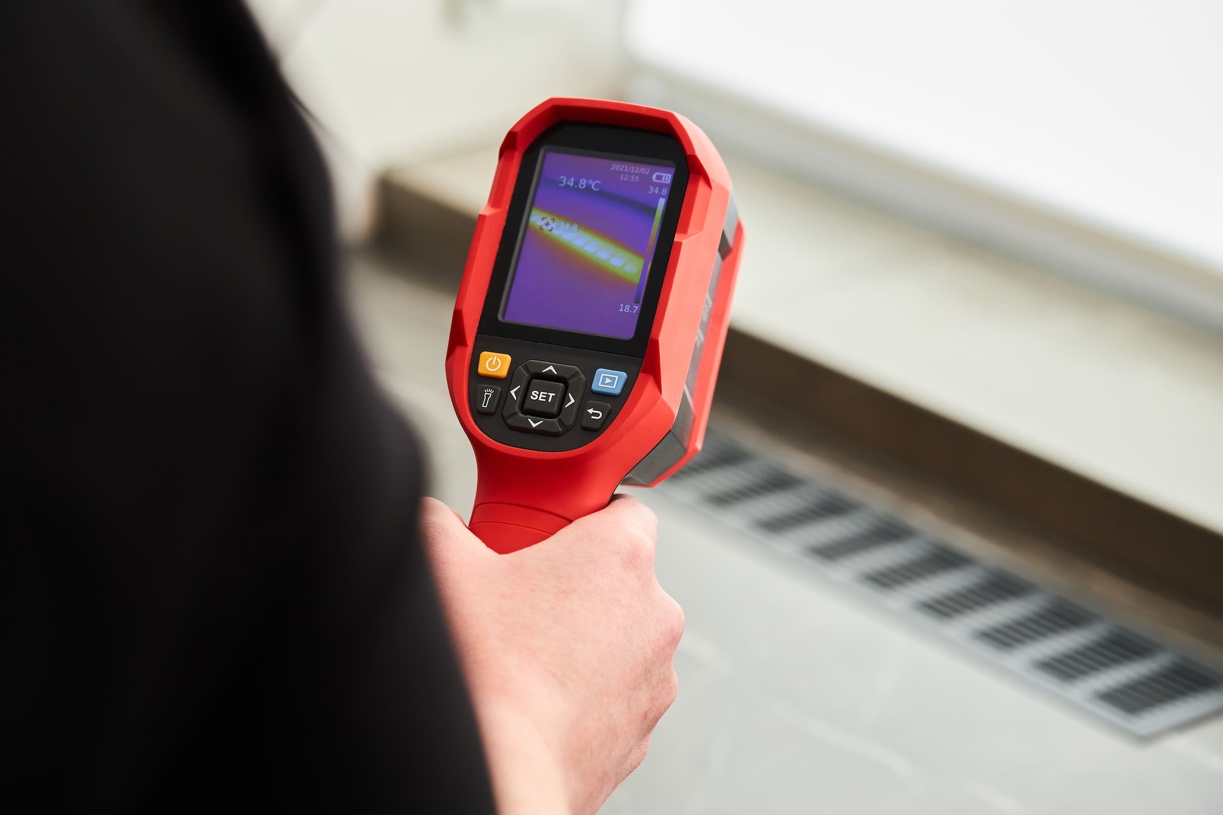 Hand holding a thermal imaging camera and pointing it at a vent in a house